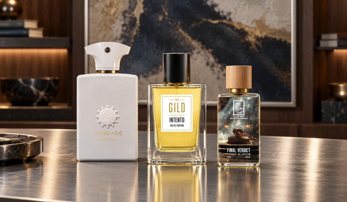 Amouage Decision, THE GILD Intento and DUA Final Verdict on a silver desk with blurred walnut shelving and navy, cream and bronze artwork.