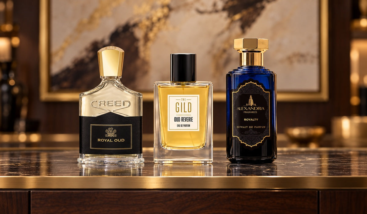 Creed Royal Oud, THE GILD Oud Reverie and Alexandria Fragrances Royalty on a luxury retail display with blurred brown and cream artwork.