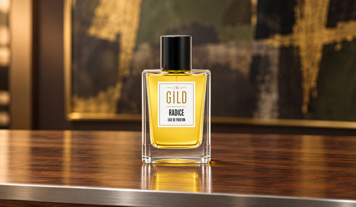 THE GILD Radice 50 ml bottle on a walnut display desk with a silver edge, in front of a blurred olive, charcoal and gold painting.