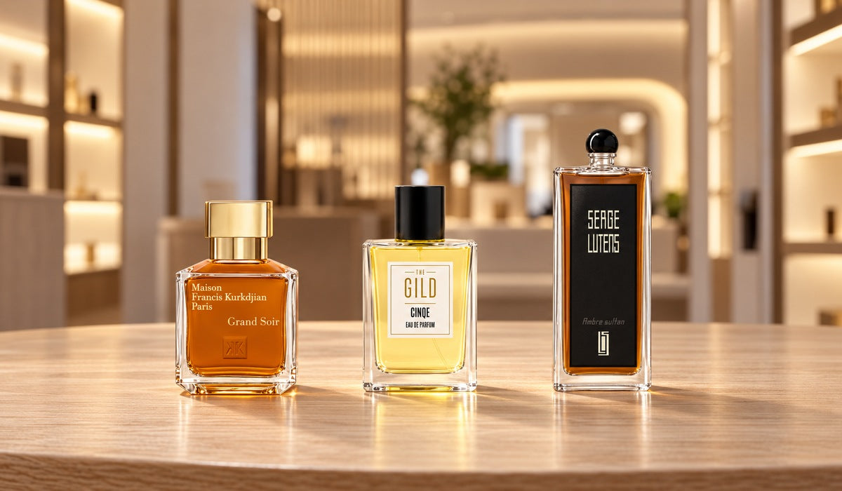 Grand Soir, THE GILD Cinqe and Ambre Sultan on a light wood table in a softly blurred fragrance store.
